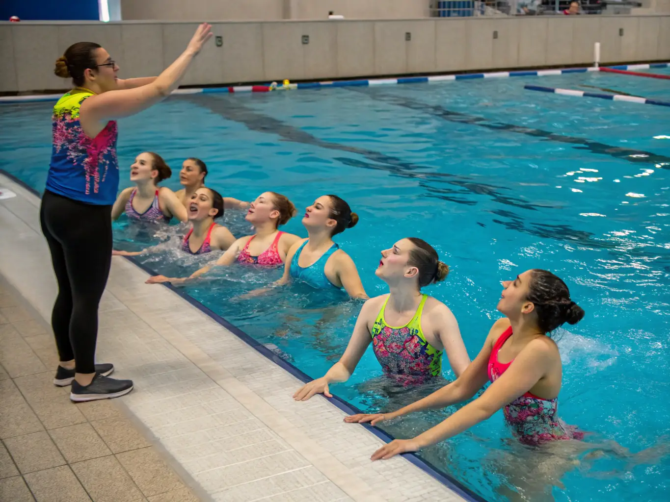 A group of diverse swimmers participating in a synchronized swimming routine, showcasing teamwork and inclusivity in a bright, indoor pool setting.